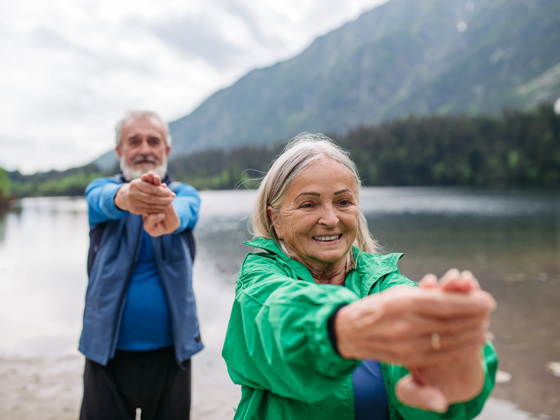 Bewegung bei Osteoporose ist zentral. Zwei Menschen dehnen ihre Handgelenke in der Natur., um Osteoporose vorzubeugen.