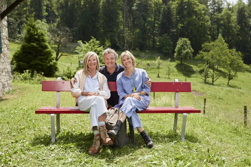 Campagne en faveur de l'activité physique : « Plus d'activité physique. Moins d'arthrose » Trois personnes sont assises sur un banc rouge en pleine nature.