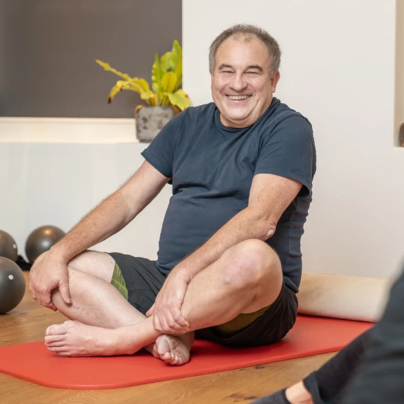 Un homme lors d'un cours de gymnastique Une personne âgée assise en tailleur lors d'un cours d'activité physique organisé par la Ligue contre les rhumatismes
