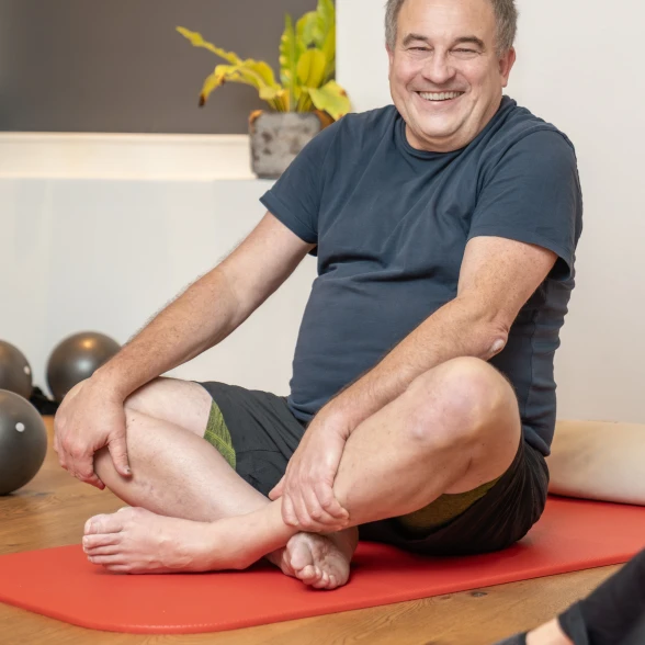 Un homme lors d'un cours de gymnastique Une personne âgée assise en tailleur lors d'un cours d'activité physique organisé par la Ligue contre les rhumatismes